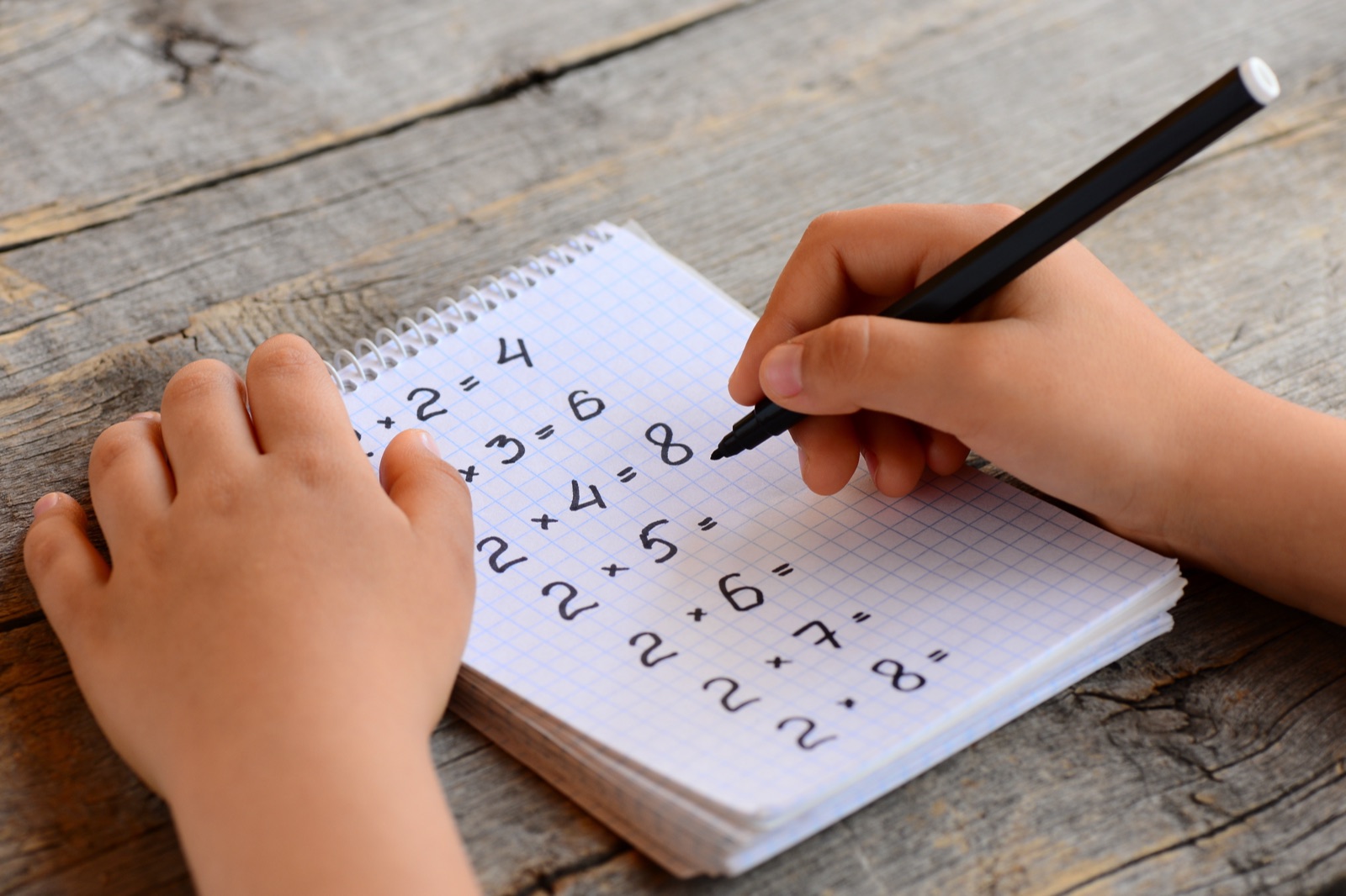 Child writing multiplication facts in a homework notebook
