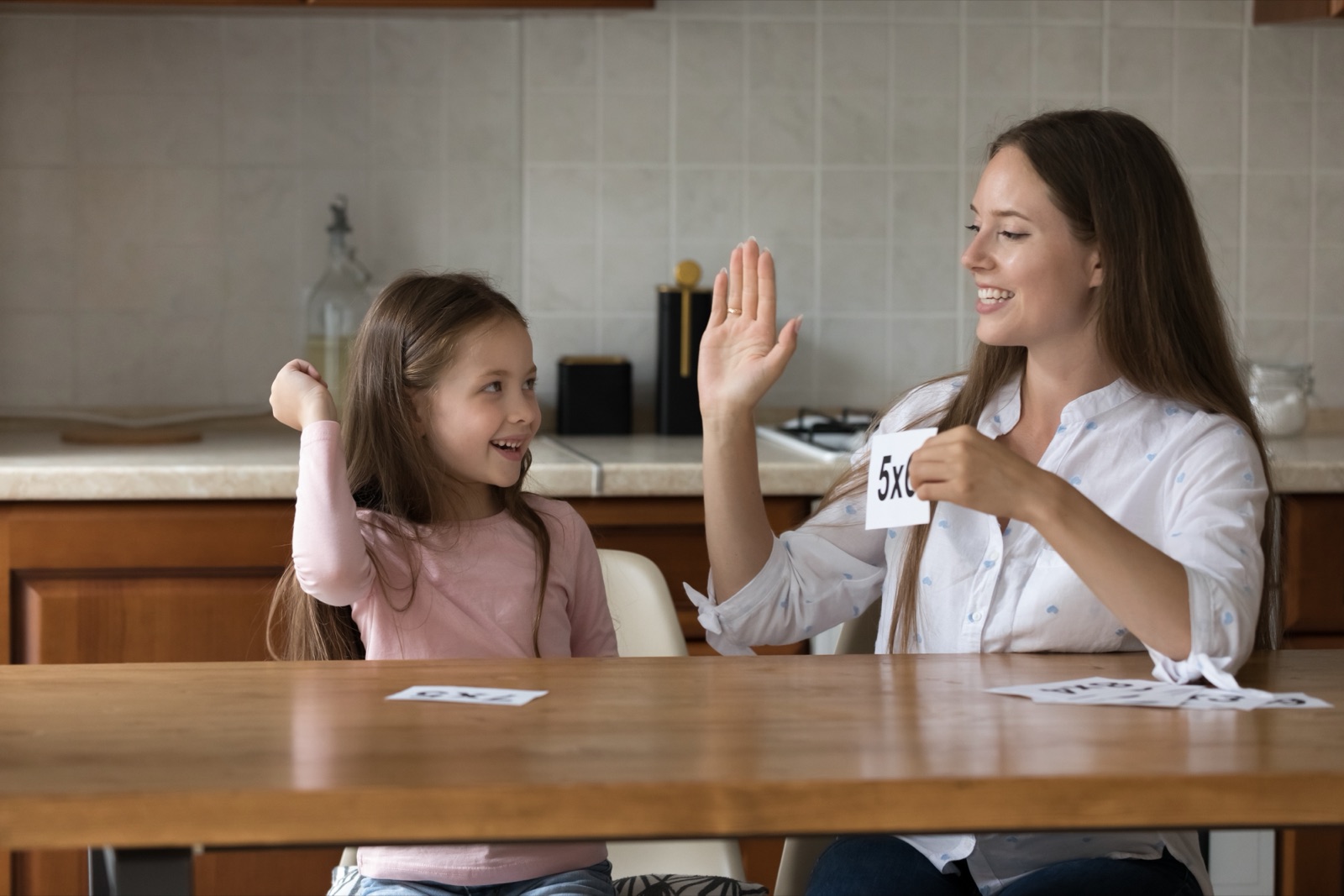 Mother helping her daughter practice multiplication flashcards at a table
