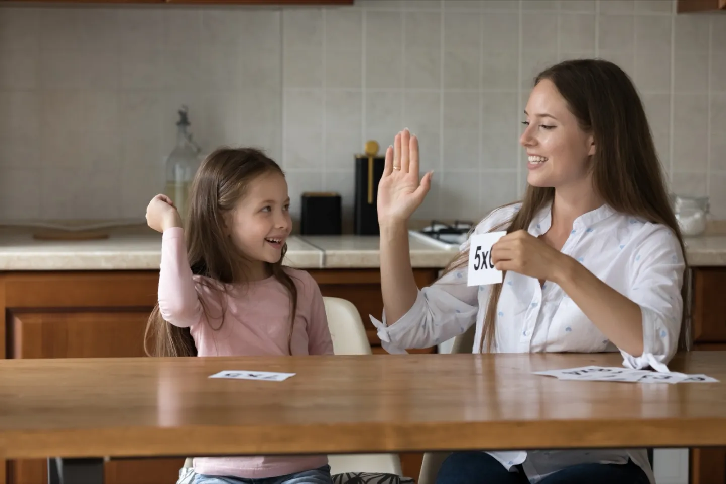 Mother helping her daughter practice multiplication flashcards at a table